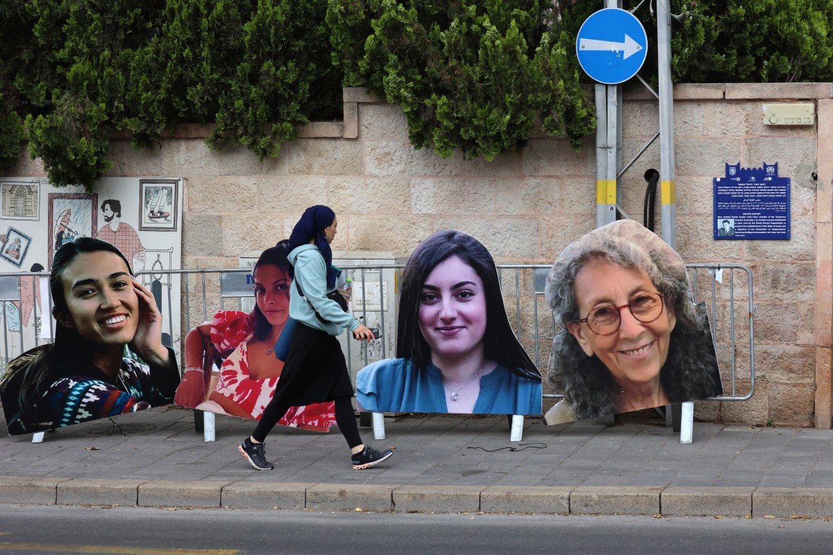 امرأة تمر أمام صور لنساء إسرائيليات محتجزات كرهائن في غزة.المصدر:AFP