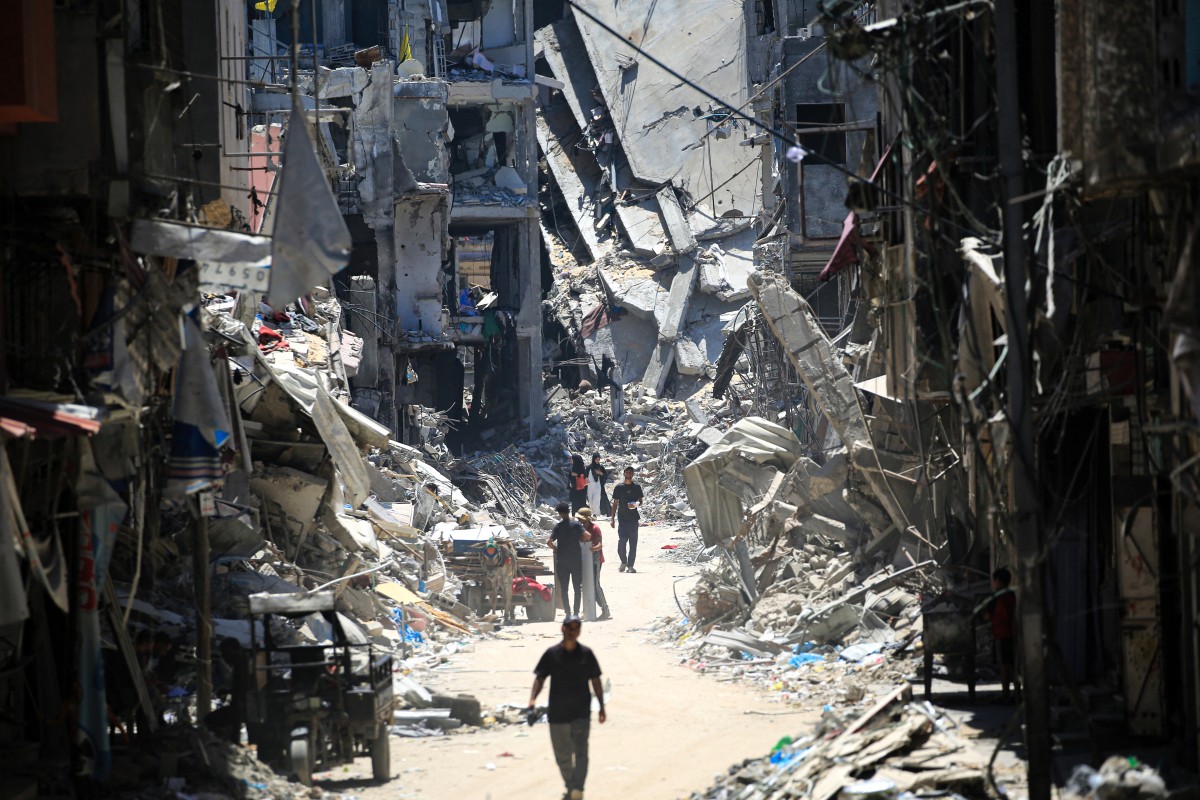 رجال فلسطينيون يسيرون في شارع ضيق بجوار المباني المدمرة في خان يونس، جنوب قطاع غزة. المصدر: AFP