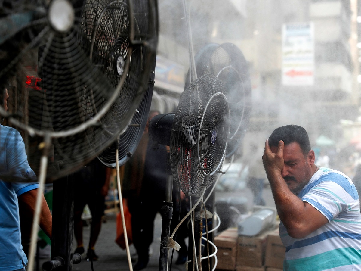 رجل يقف بجانب مراوح يرش الهواء الممزوج ببخار الماء في أحد شوارع العاصمة بغداد. المصدر ( AFP)
 

