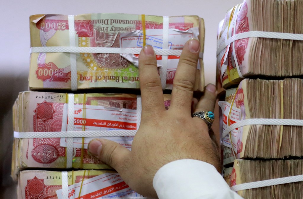 An employee arranges stacks of Iraqi dinars at currency exchange shop in Baghdad on February 14, 2023. Iraq nudged up the value of its local currency against the dollar in an effort to stabilise the dinar after tougher foreign transfer regulations sent its value fluctuating. The government adopted a new official exchange rate, fixing it at 1,300 dinars to the US dollar instead of 1,470, the prime minister's office said. (Photo by Murtaja LATEEF / AFP)