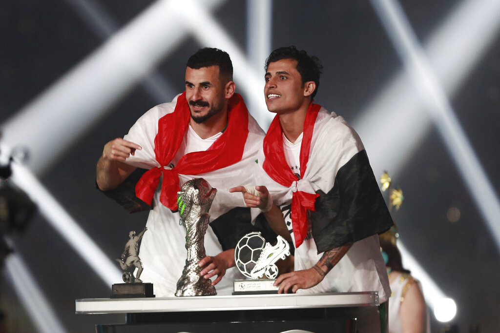 **لاعبي المنتخب العراقي أيمن حسين (يسار) وإبراهيم بايش يحتفلون بالكأس على المنصة بعد فوزهم على عمان في نهائي كأس الخليج العربي، في ملعب البصرة الدولي، البصرة، العراق، الخميس، 19 يناير 2023. العراق هزم عمان 3-2. (المصدر/ AP)