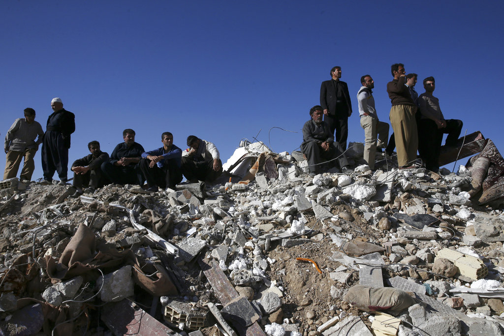 Survivors sit on the debris while rescuers search on the earthquake site in Sarpol-e-Zahab in western Iran, Tuesday, Nov. 14, 2017. (AP Photo/Vahid Salemi)