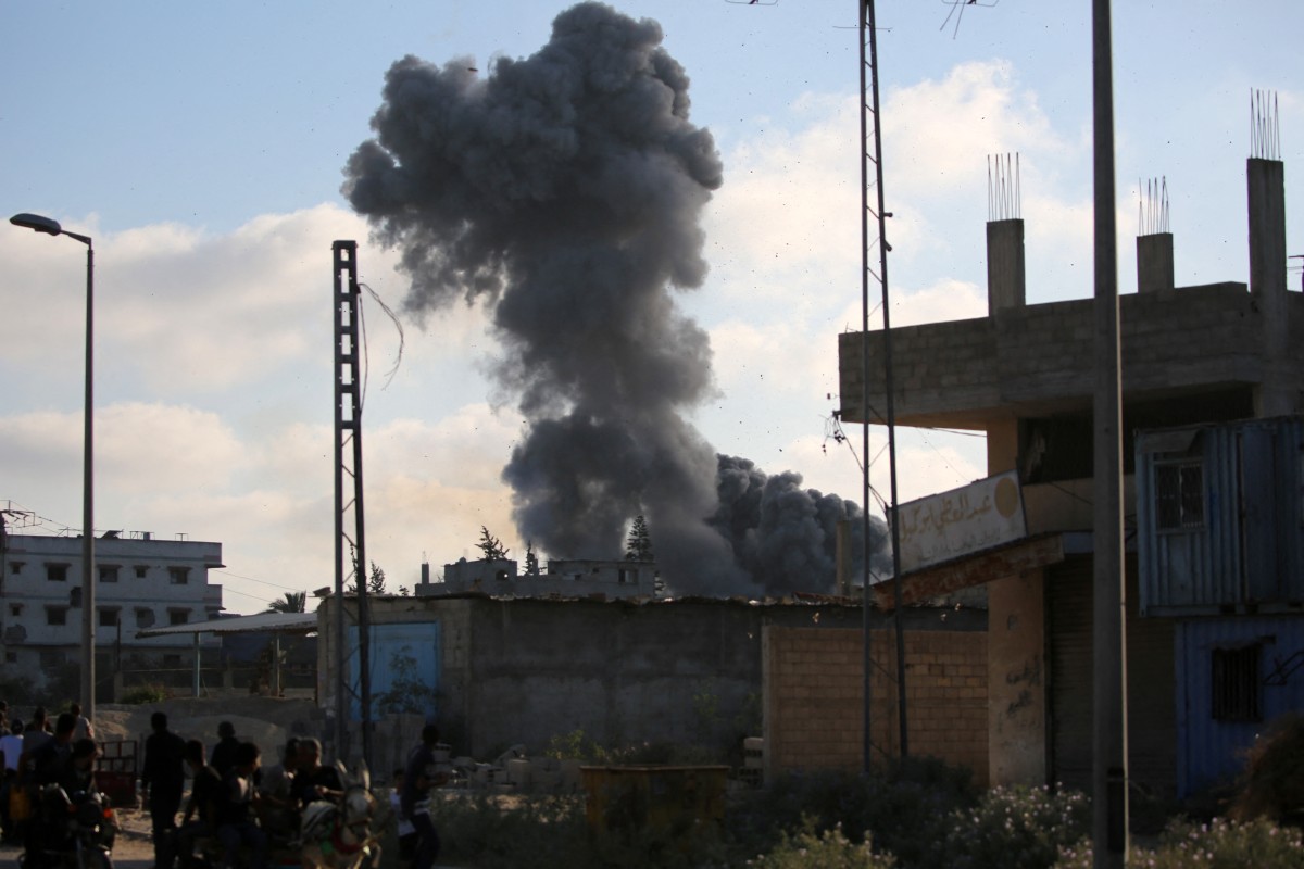 Smoke plumes rise during an Israeli strike as Palestinians walk along the Salah al-Din road near the Nusseirat refugee camp in the central Gaza Strip, used by food-seeking Palestinians to reach an aid distribution point set up by the privately-run Gaza Humanitarian Foundation (GHF), on June 25, 2025. (Photo by Eyad BABA / AFP)