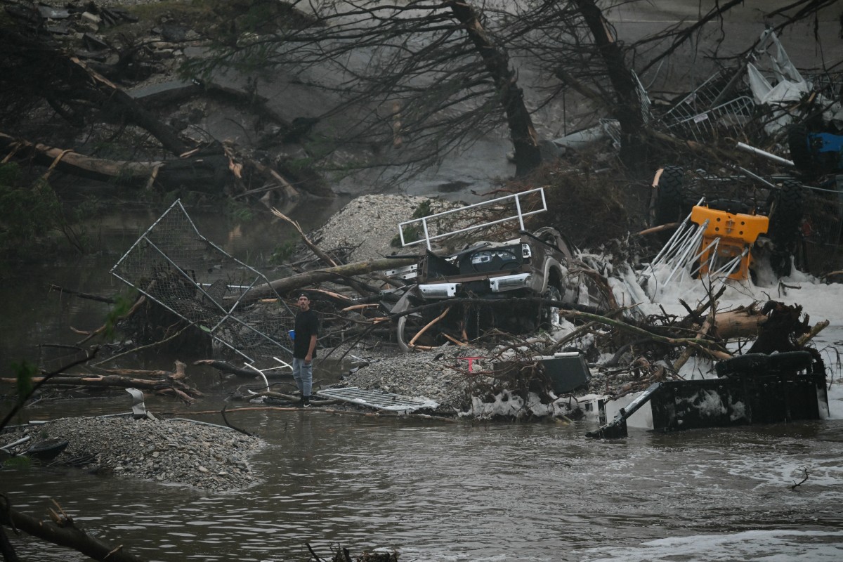 A member of the public stands next to overturned vehicles and broken trees after flooding caused by a flash flood at the Guadalupe River in Kerrville, Texas, on July 5, 2025. Rescuers were desperately searching for at least 20 girls missing from a riverside summer camp, officials said on July 5, after torrential rains caused a "catastrophic" flash flood that killed at least 24 people as it swept through south-central Texas. (Photo by RONALDO SCHEMIDT / AFP)