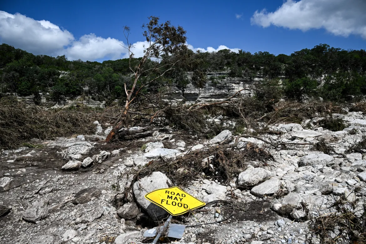 A traffic sign reading "road may flood" lies on the ground near the Guadalupe River in Hunt, Texas. [Ronaldo Schemidt/AFP]