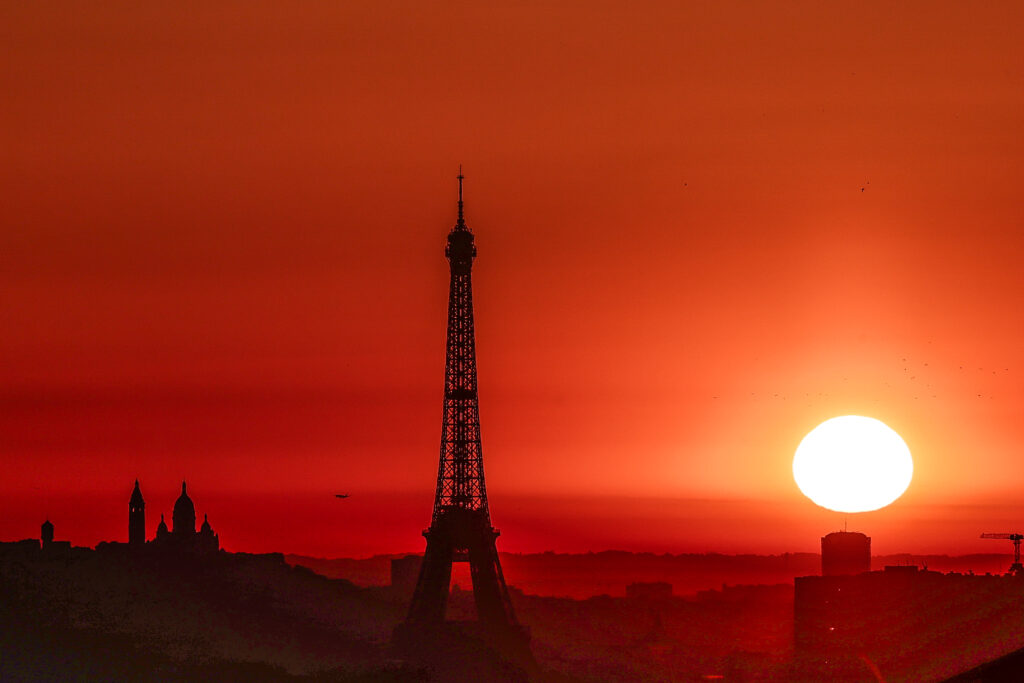 The sun rises by the Eiffel Tower and the Sacre Coeur Basilica ontop of the Montmartre hill in Paris on July 1, 2025, as the city is on red alert for high temperatures, with the top of the Eiffel Tower shut, polluting traffic banned and speed restrictions in place as a searing heatwave gripped Europe. (Photo by Thibaud MORITZ / AFP) (Photo by THIBAUD MORITZ/AFP via Getty Images)