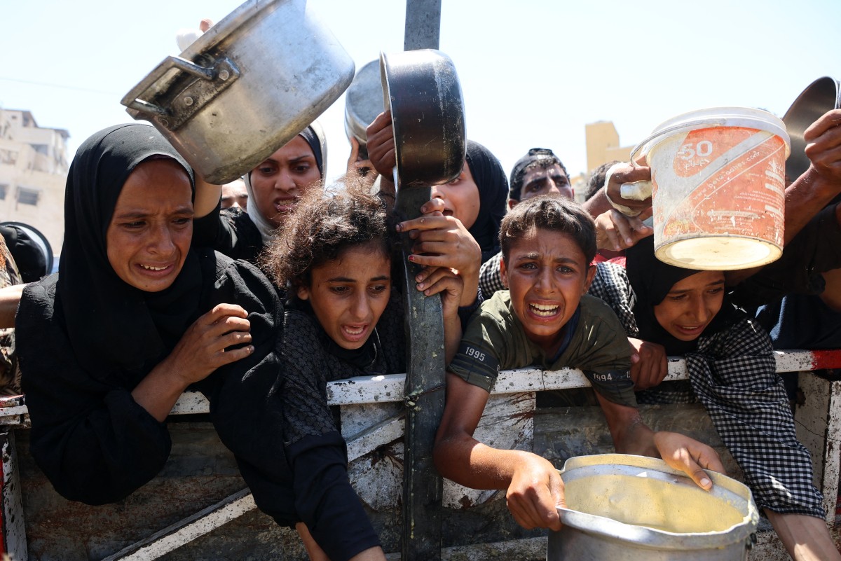 Palestinians receive lentil soup at a food distribution point in Gaza City on August 2, 2025. The World Health Organisation warned on July 27 that malnutrition was reaching "alarming levels" in Gaza. (Photo by Omar AL-QATTAA / AFP)