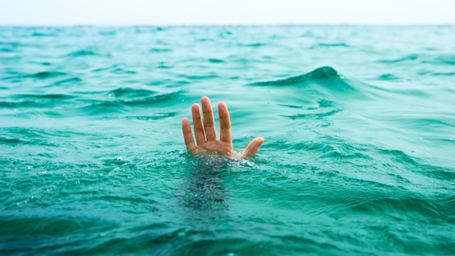 A hand stretches above the water in a symbolic depiction of drowning. 