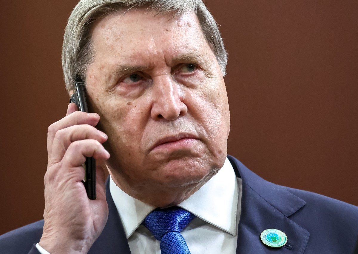 In this pool photograph distributed by the Russian state agency Sputnik, Kremlin aide Yuri Ushakov uses a smartphone as he attends a meeting of Russia's President with Iranian President in Ashgabat on December 12, 2025. (Photo by Alexander KAZAKOV / POOL / AFP)