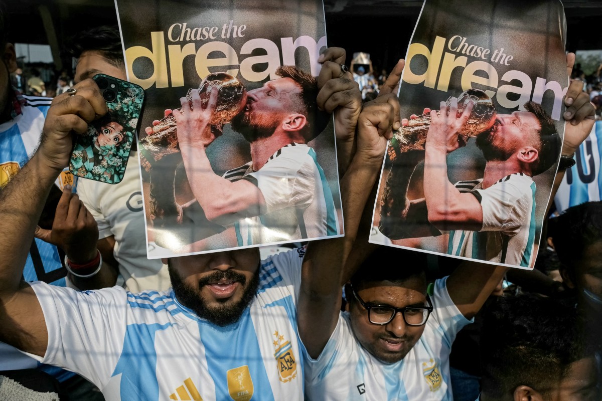 Fans hold posters of Argentinian football star Lionel Messi as they cheer from the stands before his arrival during the GOAT India Tour 2025 at the Salt Lake Stadium in Kolkata on December 13, 2025. Messi will unveil a 21-metre (70-foot) statue of himself in India on December 13, as he embarks on a three-day tour of the country that has sparked a fan frenzy. (Photo by Dibyangshu SARKAR / AFP)