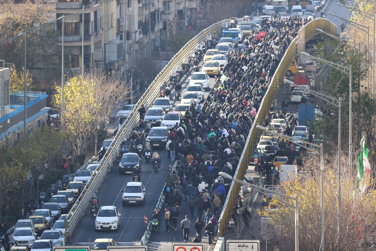 Shopkeepers and traders walk over a bridge during a protest against the economic conditions and Iran's embattled currency in Tehran on December 29, 2025.
 