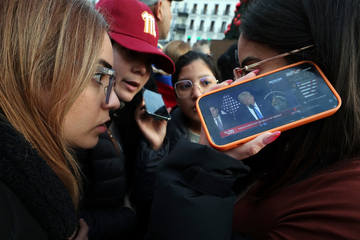Venezuelan citizens living in Spain use their smartphones to follow US' President Donald Trump's press conference as they gather at Puerta del Sol square in Madrid on January 3, 2026. 