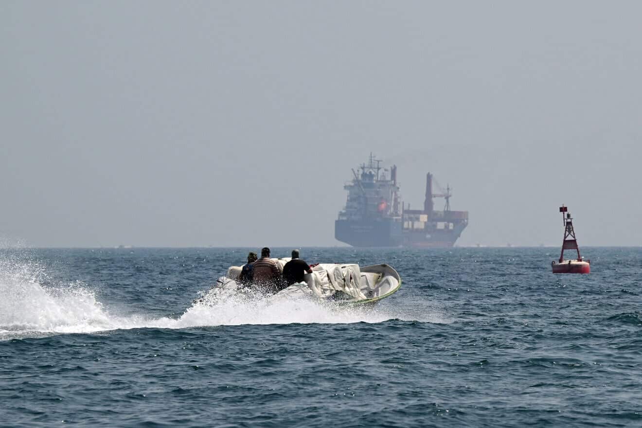 A small boat loaded with merchandise sails past the St Kitt's and Nevis-flagged container ship Marsa Victory in the waters of the Strait of Hormuz off the coast of Khasab in Oman's northern Musandam peninsula on June 25, 2025. Photo by Giuseppe Cacace/AFP via Getty Images.