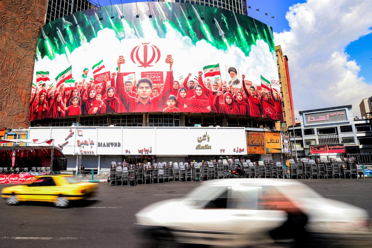Motorists drive vehicles near a large political banner, depicting missiles being fired behind Iranian demonstrators in solidarity with the government, at Valiasr Square in Tehran on April 6, 2026. Israeli strikes killed the intelligence chief of Iran's Revolutionary Guards, as the Islamic republic on April 6 defied threats from the US President to devastate civilian infrastructure if it does not reopen the Strait of Hormuz. (Photo by ATTA KENARE / AFP) /