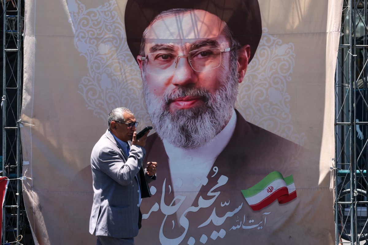 An Iranian man walks past a banner depicting Iranian supreme leader Mojtaba Khamenei at Valiasr Square in Tehran on June 15, 2026. The United States and Iran agreed a peace deal and an "immediate and permanent" end to military operations on all fronts including Lebanon, mediator Pakistan said, signaling the apparent end to more than three months of war in Middle East. (Photo by ATTA KENARE / AFP) /