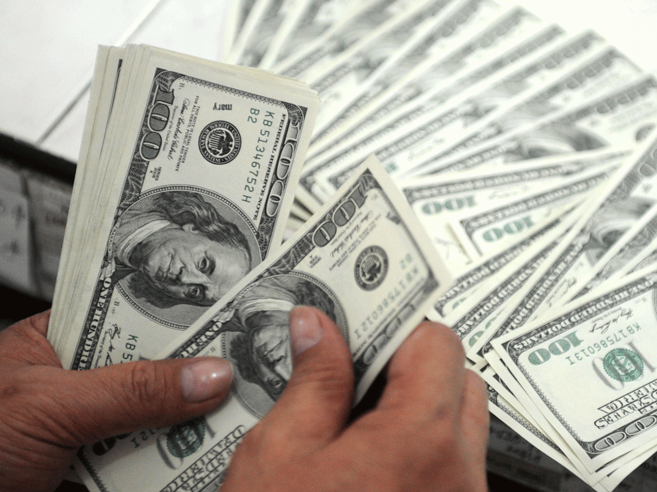 a close-up of a person's hands counting a large amount of money in United States one-hundred-dollar bills. Photo: AFP
