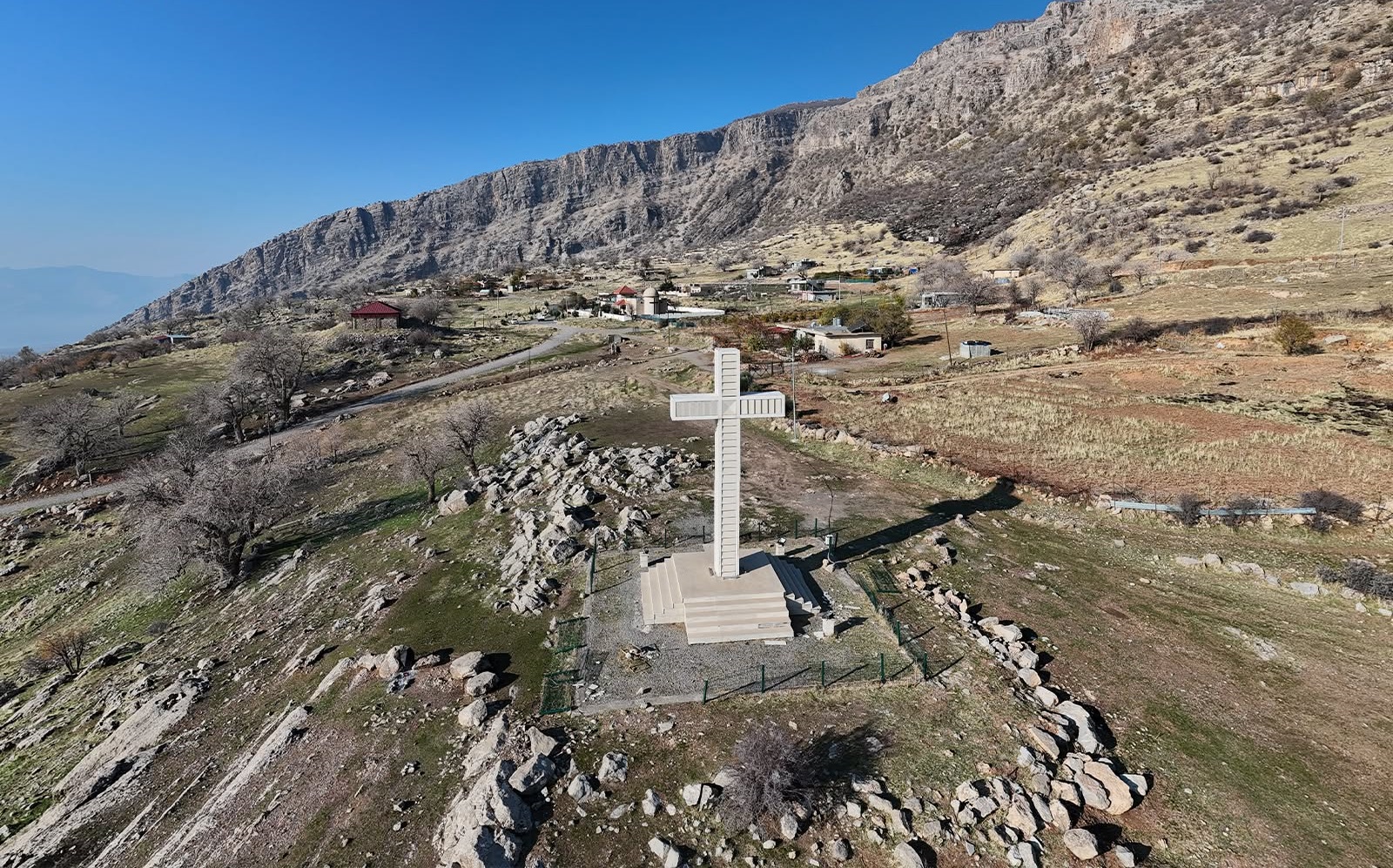 A large stone cross stands on a hillside overlooking a Christian village in the Duhok Governorate of the Kurdistan Region of Iraq.