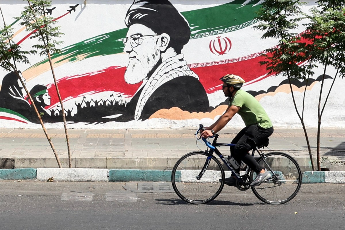 A man cycles past a mural depicting late Iranian supreme leader Ayatollah Ali Khamenei in Tehran on July 24, 2026.
 