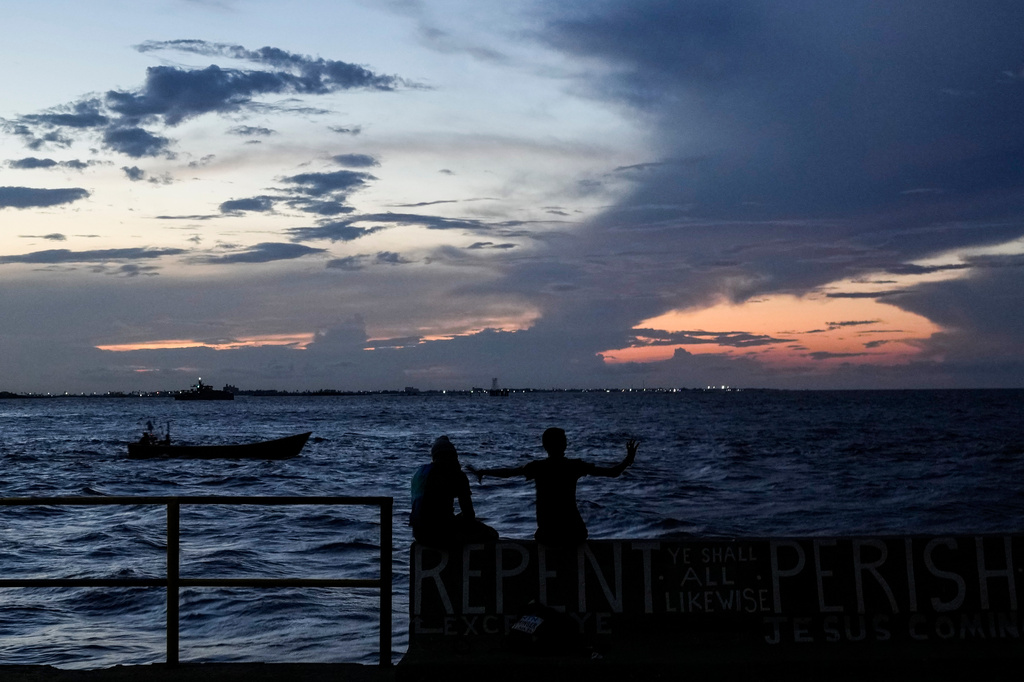 People sit on the seawall as the sun sets in Georgetown, Guyana, Tuesday, Nov. 19, 2024. (AP Photo/Matias Delacroix, File)