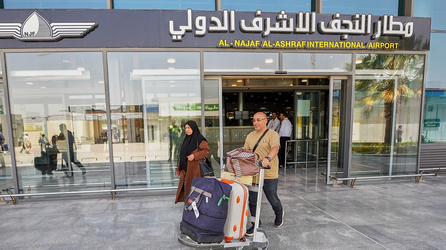 دوو گەشتیار لەبەردەم دەروازەی سەرەکی فڕۆکەخانەی نەجەف