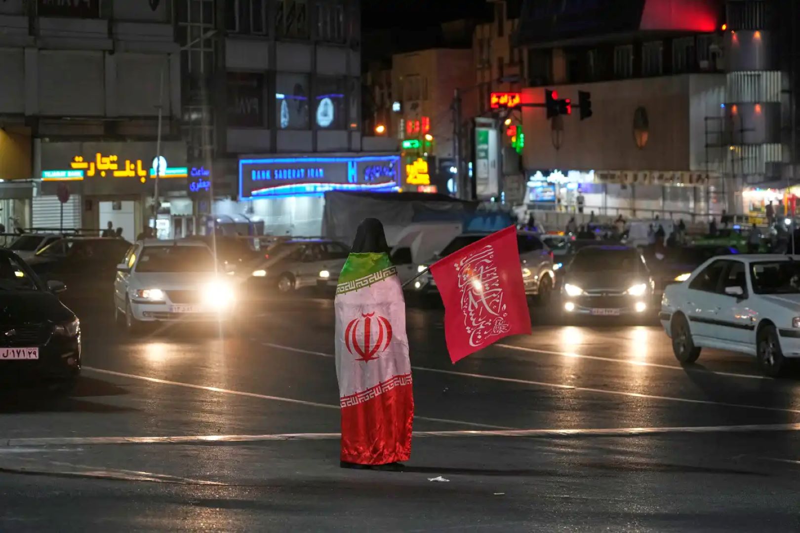 یک تظاهرکننده طرفدار دولت، در حالی که پرچم مذهبی را در دست دارد، پرچم ایران را بر تن دارد و در مراسم بزرگداشت رهبر ایران، آیت‌الله علی خامنه‌ای، در میدانی در تهران، ایران، شنبه، ۱۱ ژوئیه ۲۰۲۶، شرکت کرده است. (عکس از آسوشیتدپرس/وحید سالمی)
